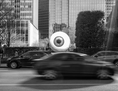 Giant eyeball sculpture on a city street with cars.