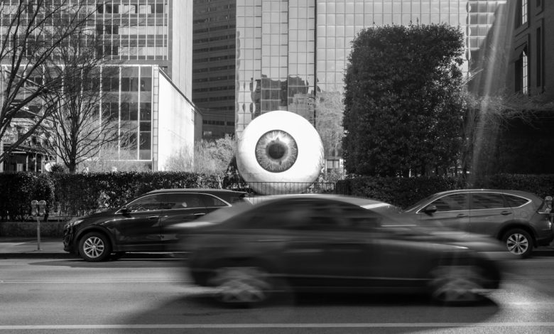 Giant eyeball sculpture on a city street with cars.