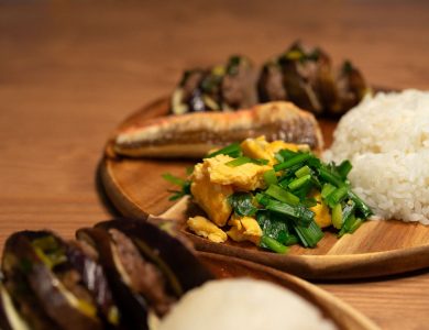 Delicious Asian meal featuring rice, vegetables, and grilled fish on a wooden plate.