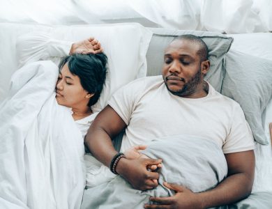 From above of romantic diverse couple holding hands while sleeping in comfortable bed at home in morning