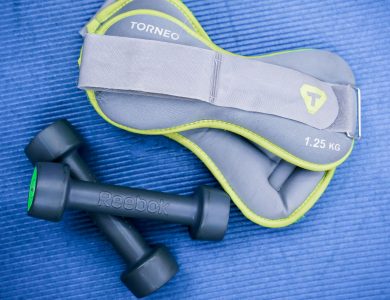 From above of modern dumbbells and leg weight belts placed on blue fitness mat in studio