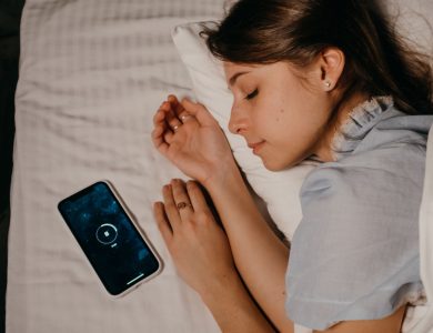 A woman peacefully sleeps in bed with a smartphone beside her, illustrating modern bedtime habits.