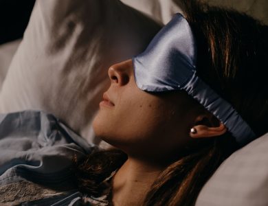 A woman peacefully sleeping on a pillow with a blue silk eye mask, indoors.