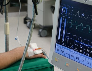 A close-up of a patient's hand connected to medical equipment in an ICU room.