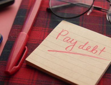 a note that says pay debt next to a pen and glasses