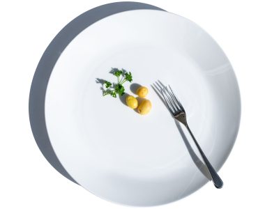 Minimalist still life of potatoes and parsley on a white plate with fork, symbolizing dieting.