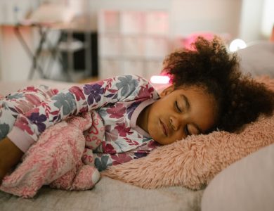 A young girl in floral pajamas peacefully sleeping with toys in a comfortable bedroom setting.