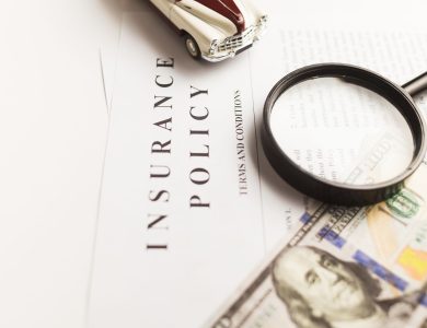 Close-up image of an insurance policy with a magnifying glass, money, and toy car.