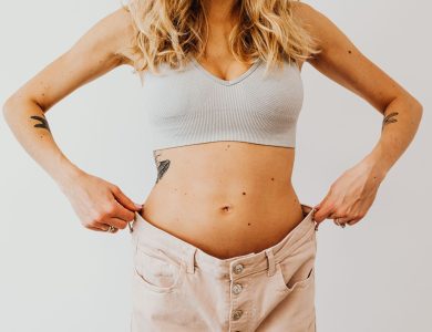 A woman displaying weight loss by wearing oversized pants and crop top, showing tattoos.