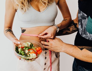 A couple measuring waistline with a tape and holding a fresh salad bowl, focusing on fitness and weight loss.