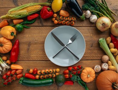 Top view of fresh vegetables creatively arranged around an empty plate on a wooden table.