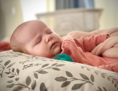 A serene newborn baby sleeping on a patterned pillow indoors, wrapped in a soft blanket.