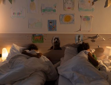 Two children asleep in a cozy bedroom with wall drawings, soft lighting, and comforting decor.