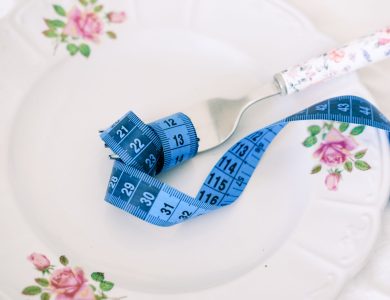 A floral plate with a fork and blue measuring tape symbolizing dieting or healthy eating.