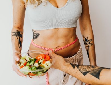 Fit woman measuring waist while holding a healthy salad bowl