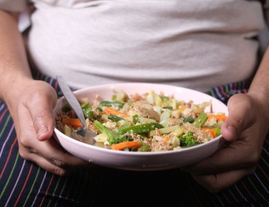 Close-up of an overweight individual holding a nutritious vegetable salad in a pink bowl.
